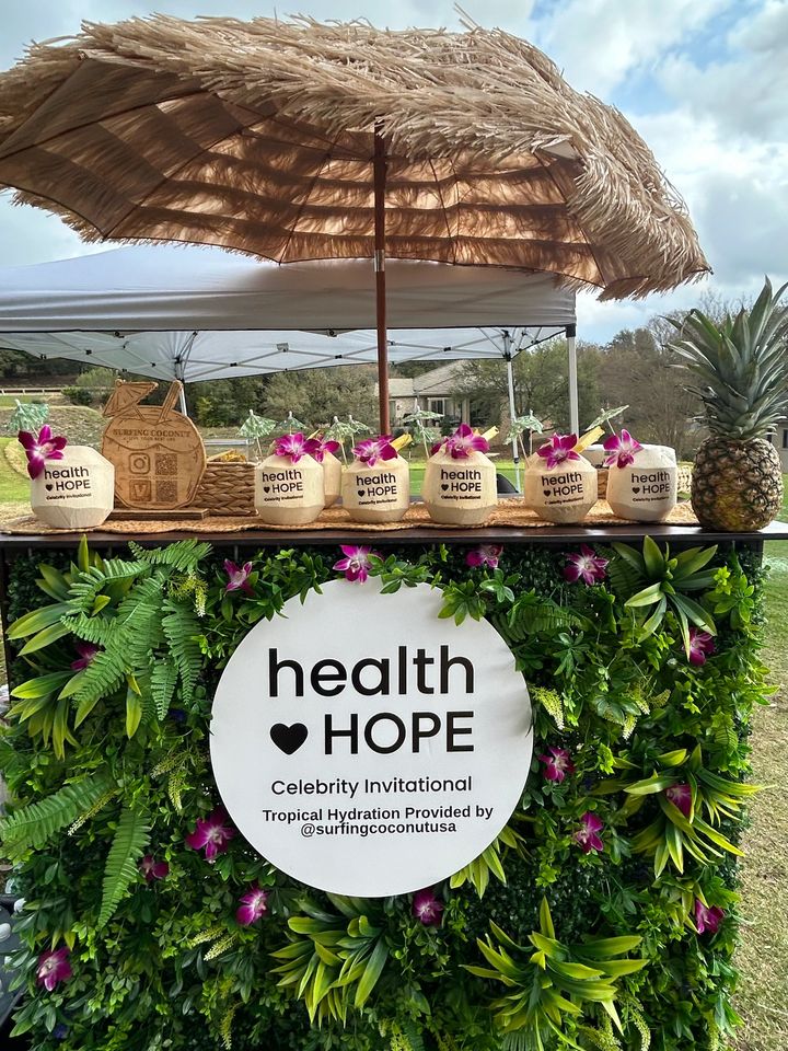 Surfing Coconut stand with flower-topped fresh coconuts under a thatched umbrella at an event